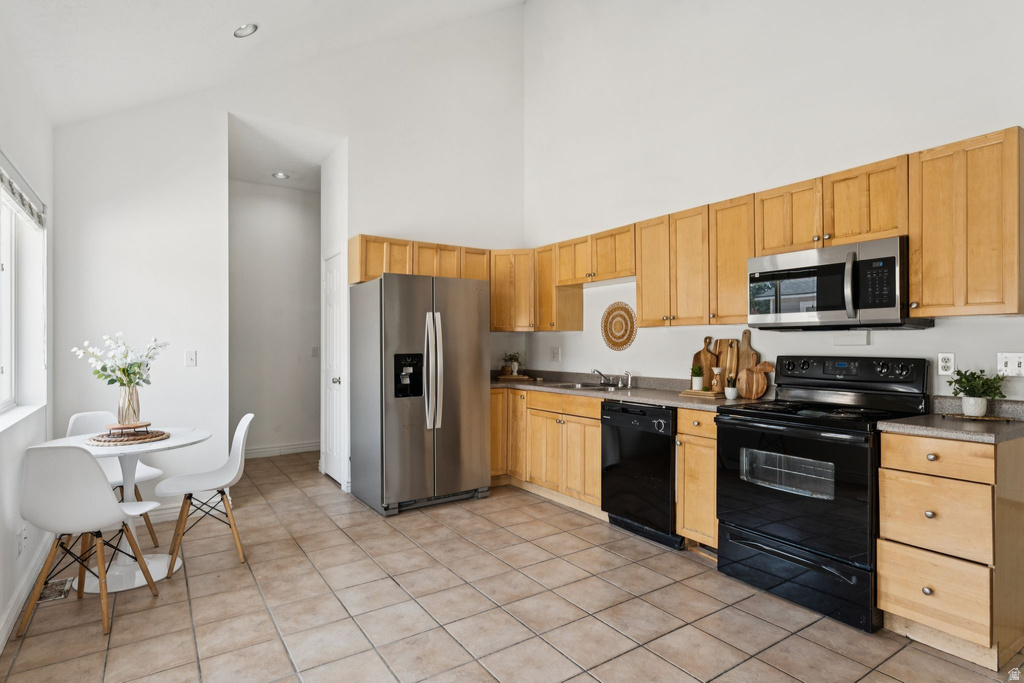 Kitchen featuring black appliances, lofted ceiling, light wood finish cabinets, and light tile patterned floors