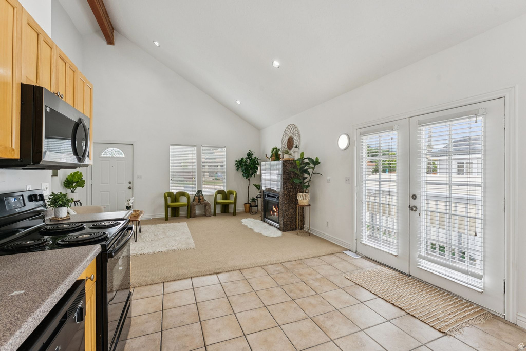 Kitchen featuring black appliances, a glass covered fireplace, light carpet, lofted ceiling, and french doors