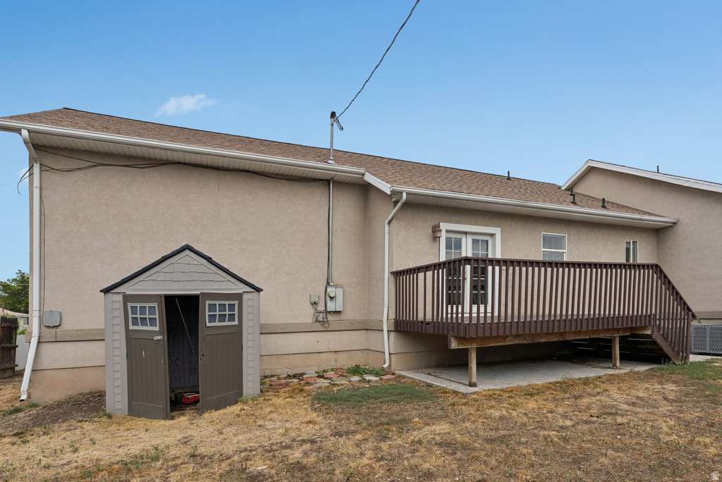 Back of property featuring a storage shed, a wooden deck, stucco siding, and a shingled roof
