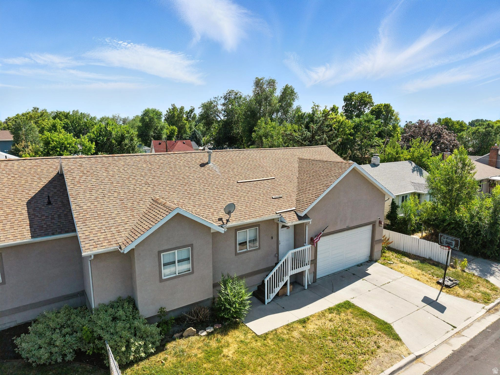 Ranch-style house with stucco siding, a shingled roof, and view of scattered trees
