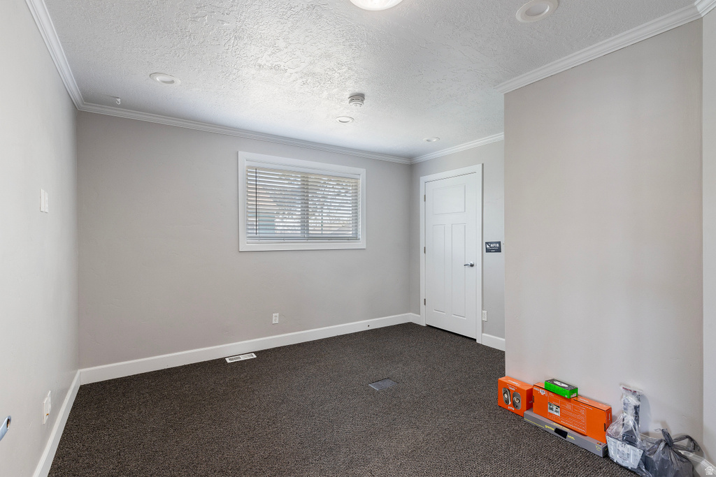Spare room with dark colored carpet, ornamental molding, and a textured ceiling