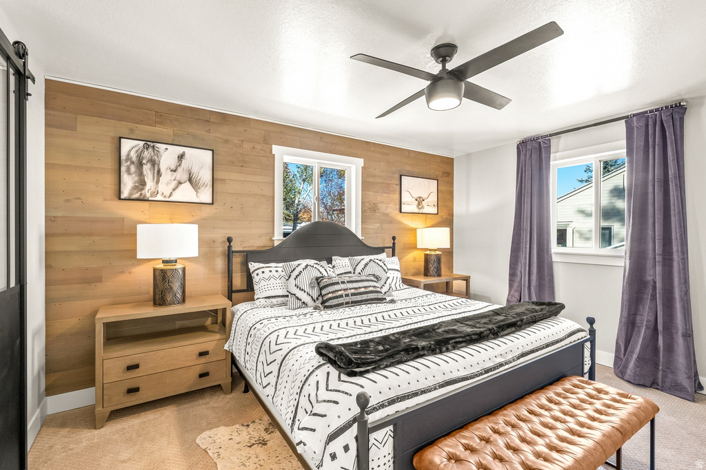 Bedroom featuring light colored carpet, a barn door, wood walls, and ceiling fan