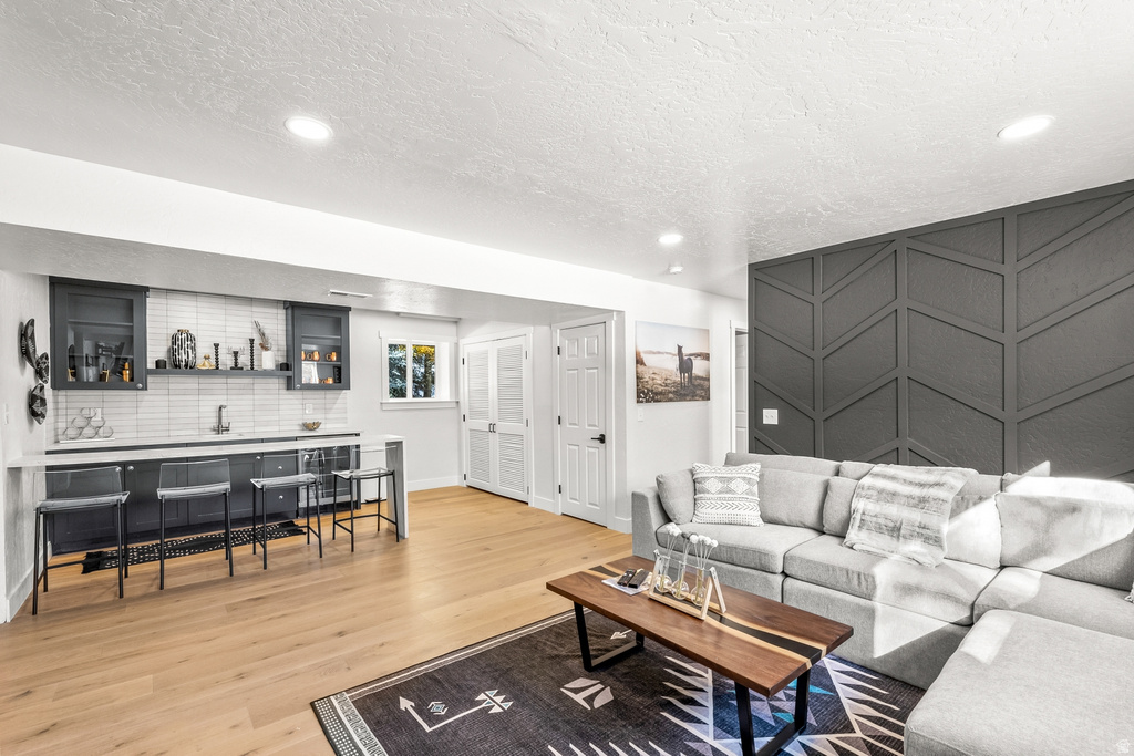 Living area featuring light wood finished floors, bar with sink, a textured ceiling, beverage cooler, and recessed lighting