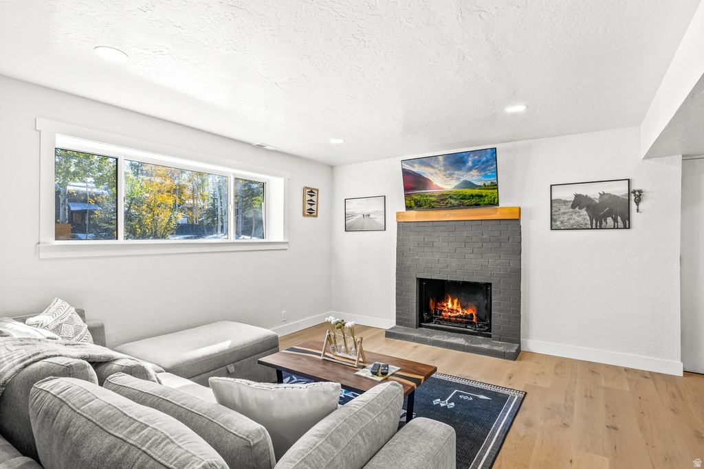 Living area with a brick fireplace, light wood-style floors, recessed lighting, and a textured ceiling