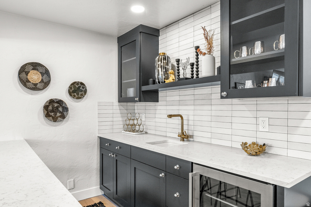 Bar with light stone countertops, open shelves, wine cooler, decorative backsplash, and glass fronted cabinets