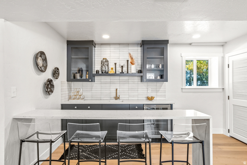 Indoor wet bar with wine cooler, light stone counters, glass fronted cabinets, recessed lighting, and a textured ceiling