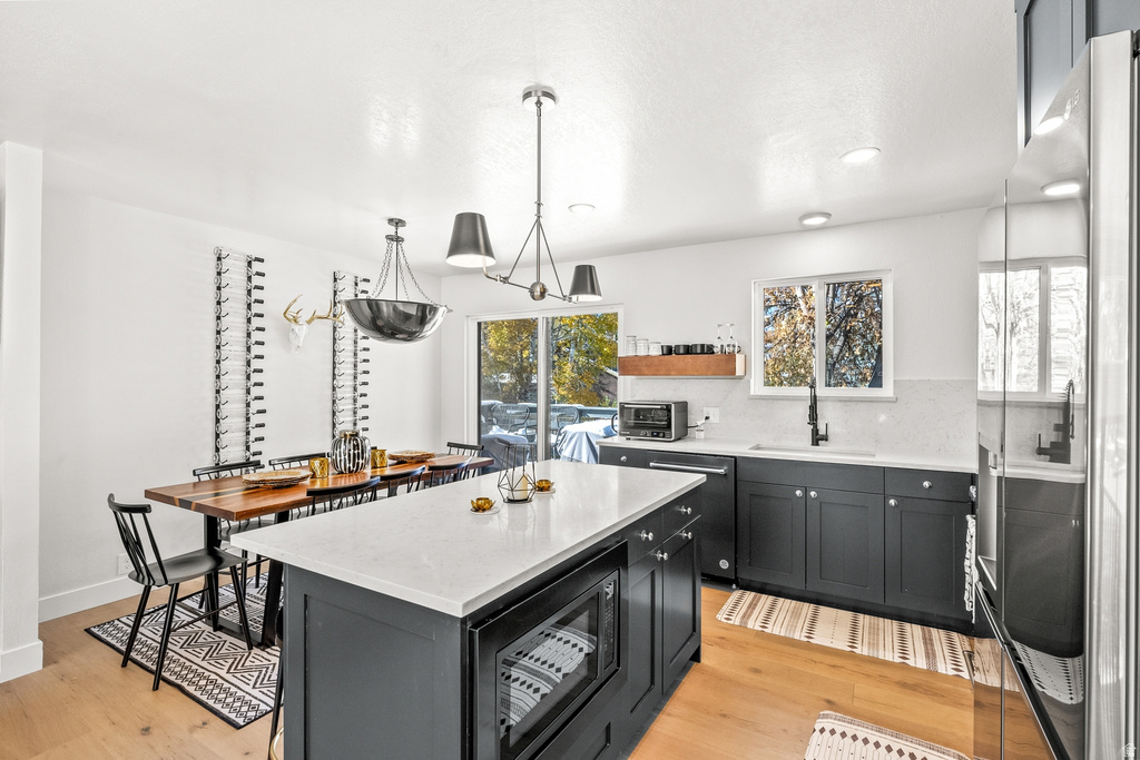Kitchen featuring dark cabinetry, freestanding refrigerator, light wood finished floors, a center island, and open shelves