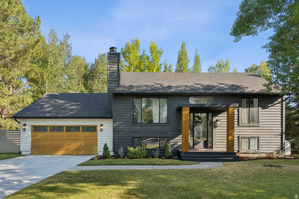 Raised ranch featuring a front yard, a chimney, driveway, and an attached garage