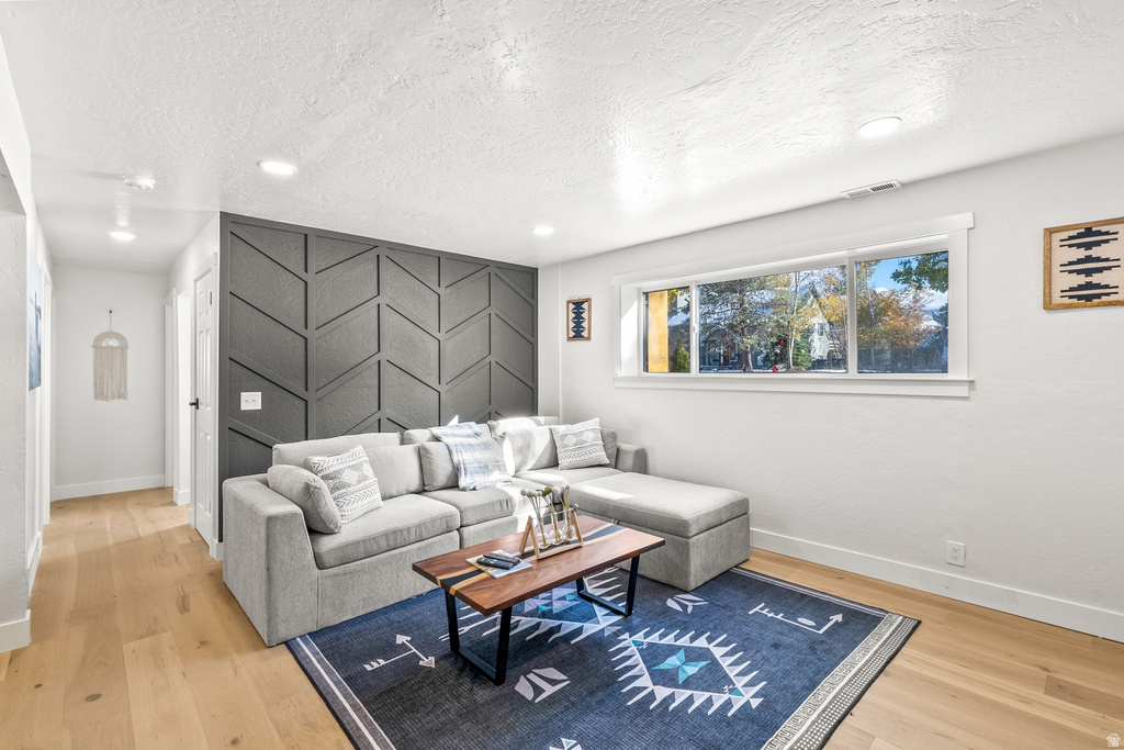 Living room featuring an accent wall, light wood-style flooring, a textured ceiling, and recessed lighting