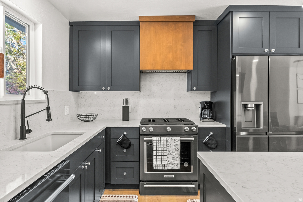 Kitchen with stainless steel appliances, light stone countertops, decorative backsplash, and range hood