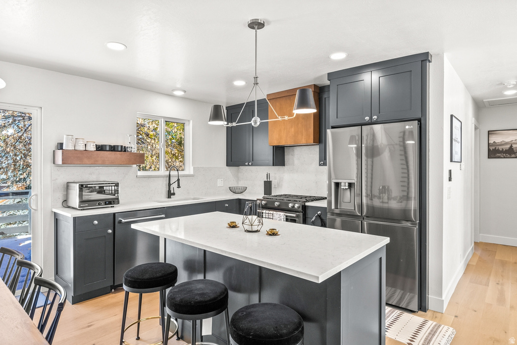 Kitchen with stainless steel appliances, a breakfast bar area, backsplash, a kitchen island, and light wood-style flooring