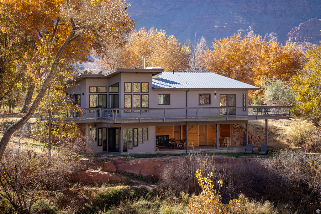 Back of house featuring a wooden deck, a patio area, stucco siding, and a metal roof