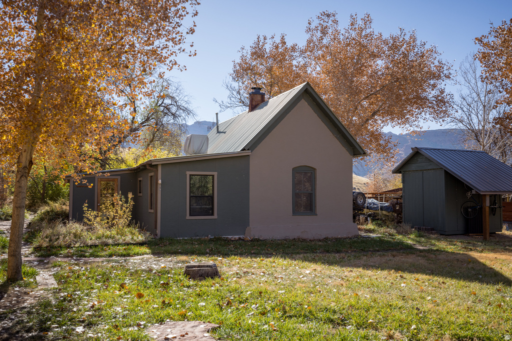 View of property exterior with a chimney, a yard, a metal roof, stucco siding, and a storage unit