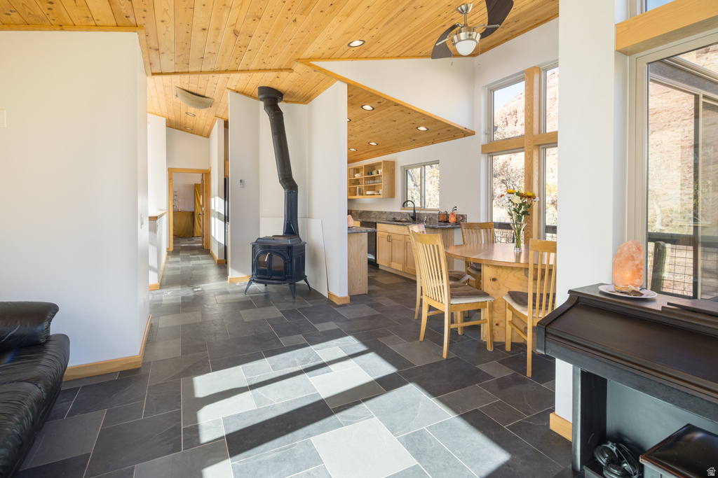 Dining space with a wood stove, wood ceiling, a towering ceiling, recessed lighting, and stone tile flooring