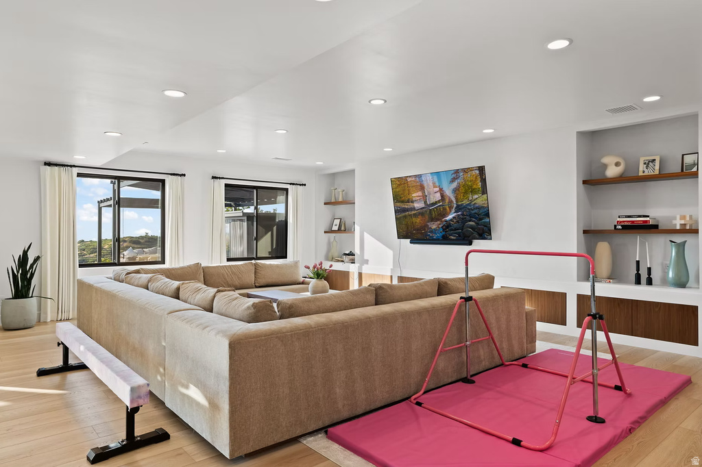 Living room with built in features, light wood-type flooring, and recessed lighting