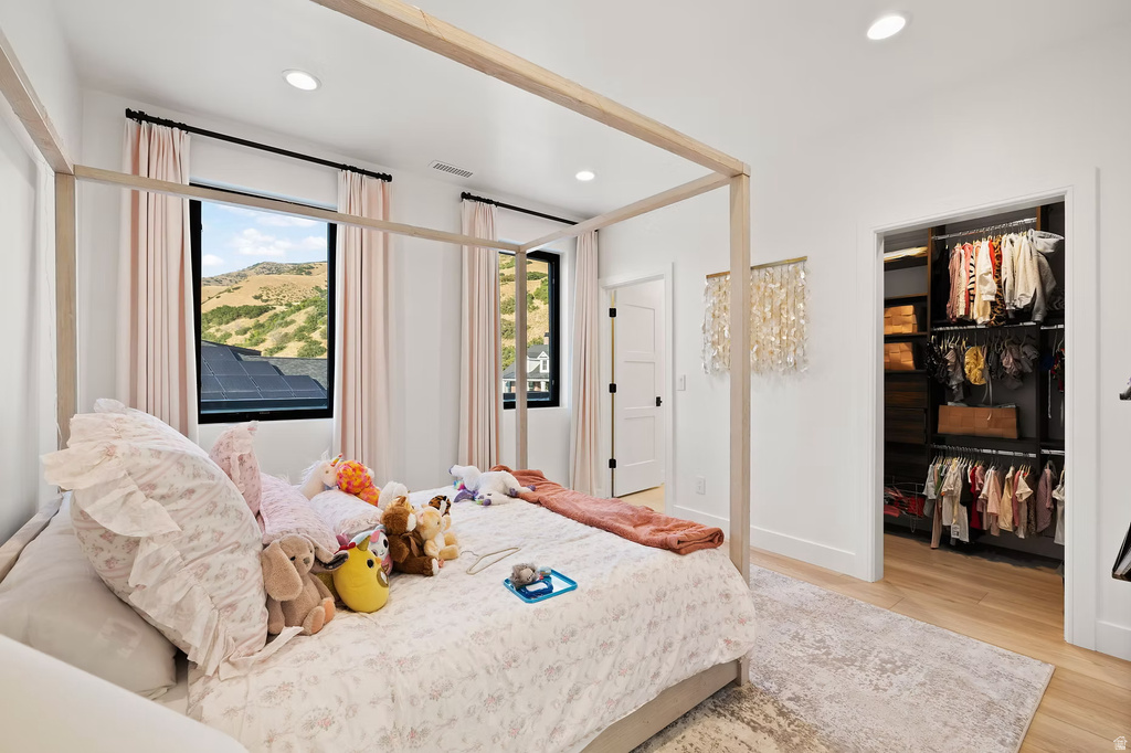 Bedroom with light wood finished floors, a spacious closet, and recessed lighting