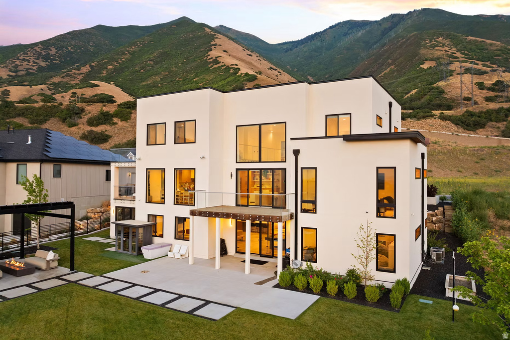 Rear view of house with a mountain view, a lawn, a patio area, and stucco siding