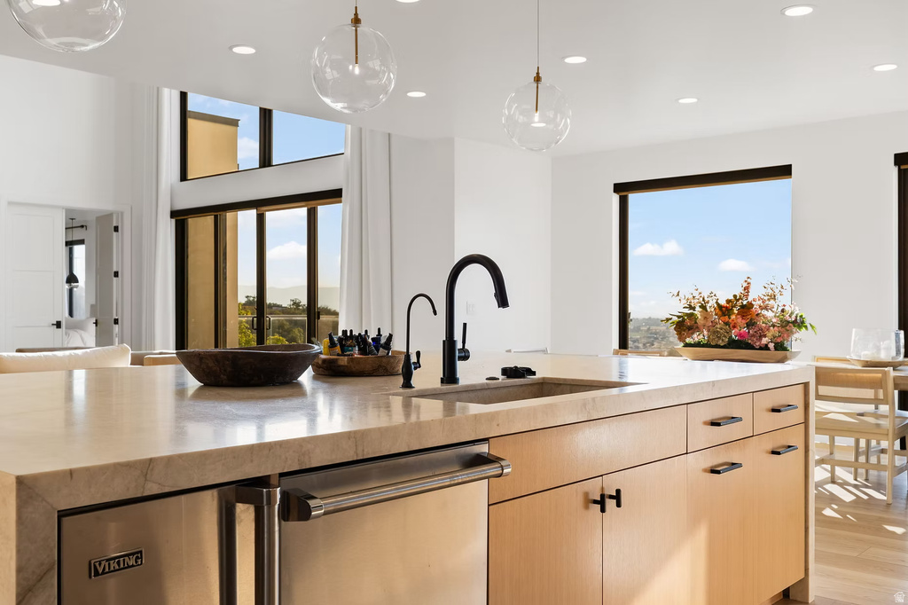 Kitchen featuring light wood finish cabinetry, light stone counters, dishwasher, pendant lighting, and light wood finished floors