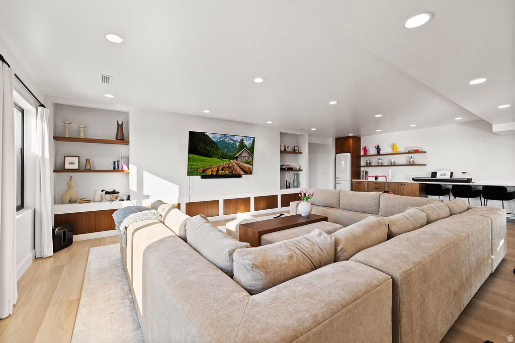 Living room featuring light wood finished floors, built in features, recessed lighting, and bar with sink