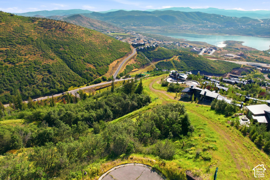 Hilly terrain with lush greenery, featuring a winding road and distant water body