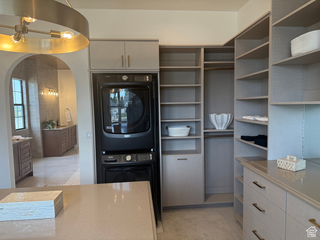 Integrated laundry area featuring stacked appliances within custom cabinetry, extensive built-in shelving, multiple drawers with gold-tone hardware, and a center island with a stone-finish countertop