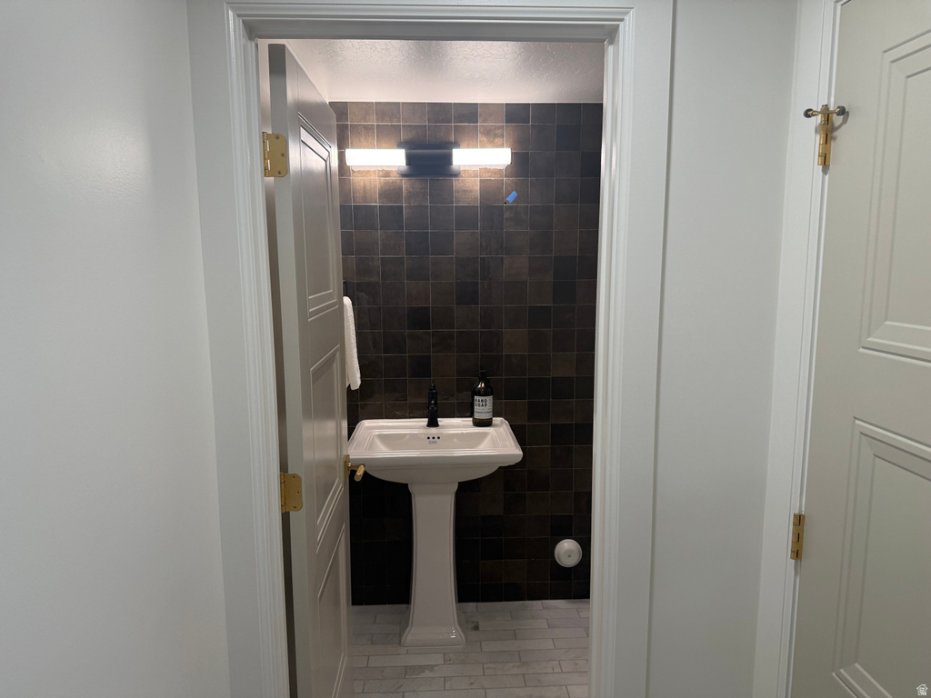 Pedestal sink with a black faucet set against a dark tiled accent wall
