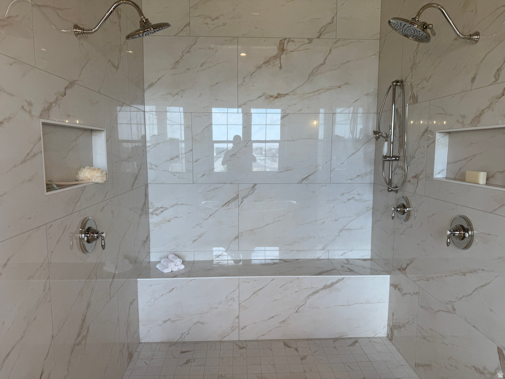 Spacious walk-in shower with large-format tile, dual rain shower heads, a built-in bench, and integrated recessed shelving