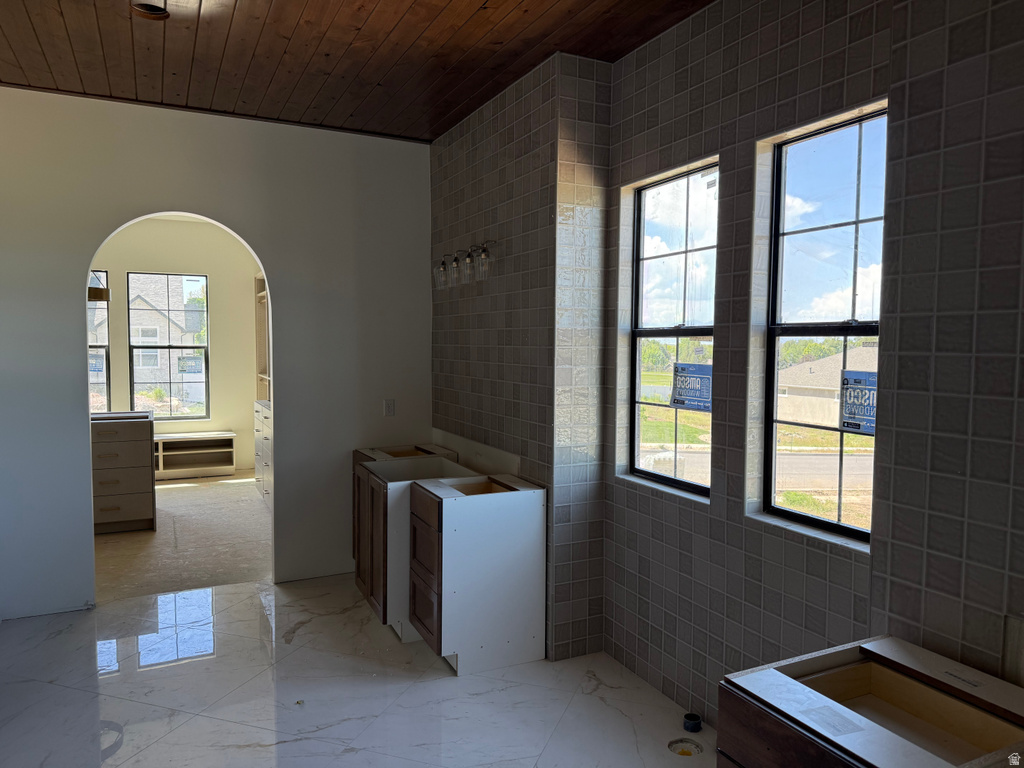 Bathroom featuring a wood-finish ceiling, large format tile flooring, and a tiled accent wall with two windows