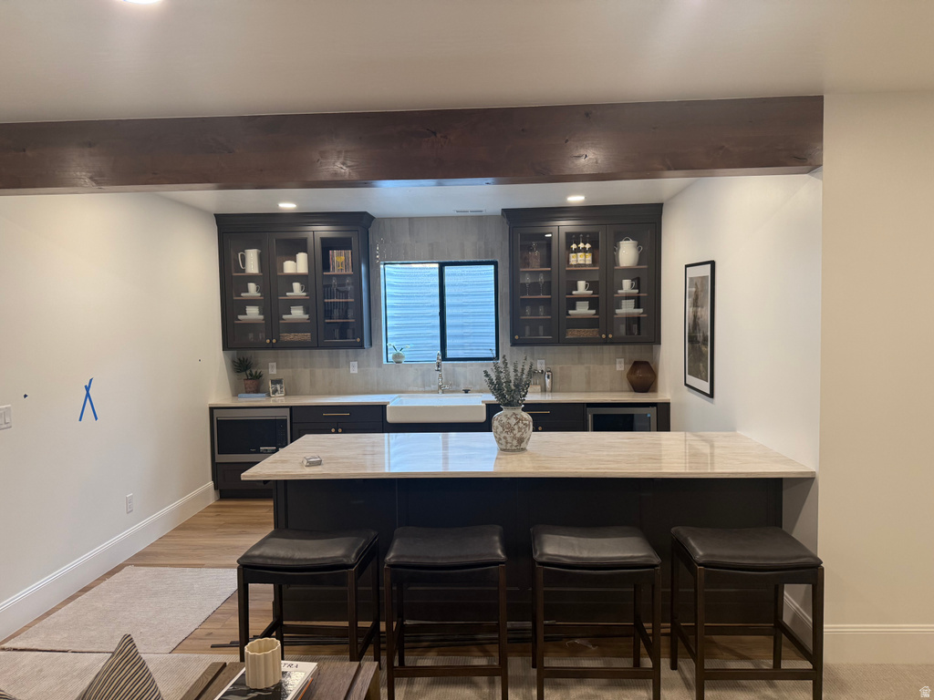 Wet bar featuring dark cabinetry, a farmhouse sink, and integrated under-counter appliances