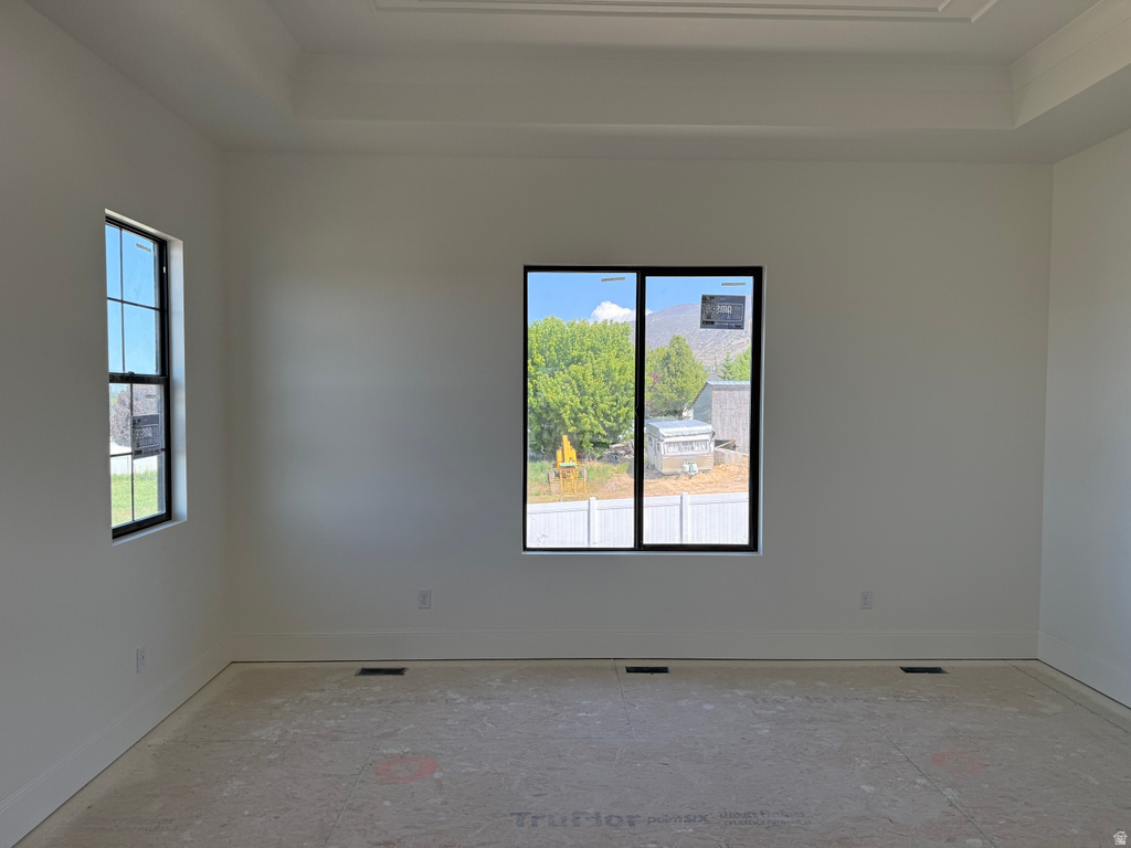 Spacious room featuring a tray ceiling, multiple windows with black frames, white baseboards, and unfinished subflooring