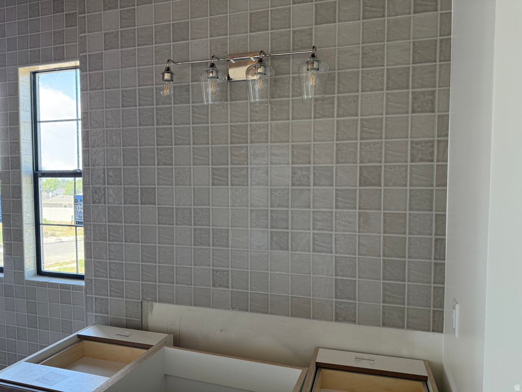 Bathroom featuring square mosaic wall tile, a three-light vanity fixture with clear glass shades, and window with dark trim