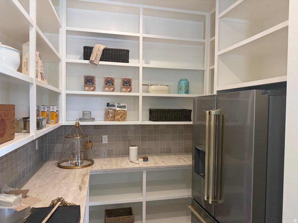 Built-in pantry with extensive shelving, L-shaped countertop, mosaic tile backsplash, and integrated stainless steel refrigerator