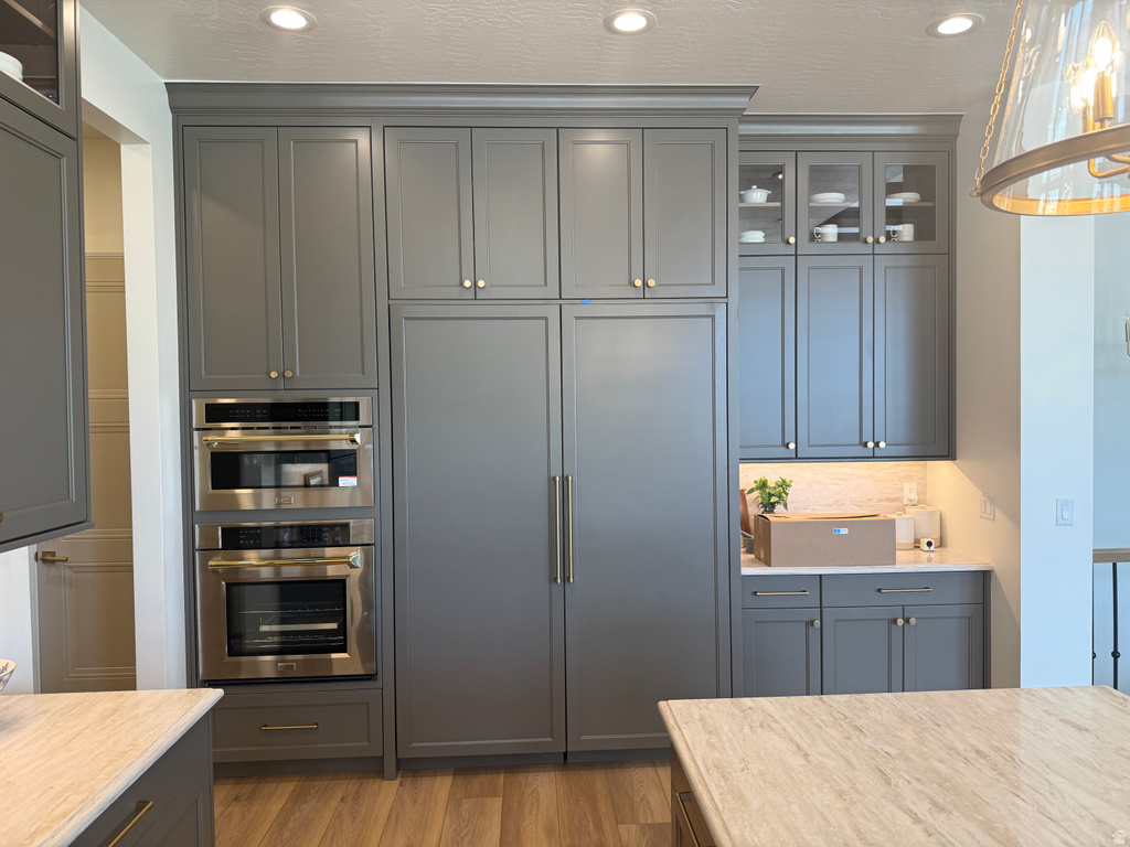 Modern kitchen featuring floor-to-ceiling gray cabinetry with gold-finish hardware, integrated stainless steel double ovens, and a built-in refrigerator