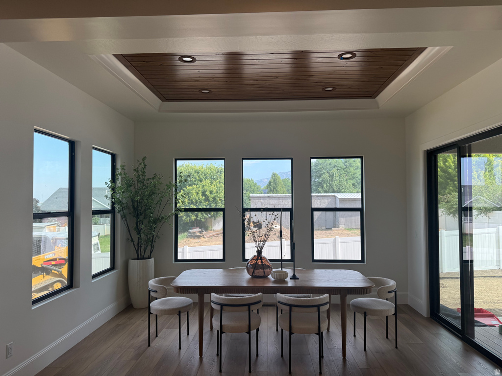 Dining area featuring a wood-finish tray ceiling with recessed lighting, multiple black-framed windows, a large glass sliding door, and wood-finish flooring