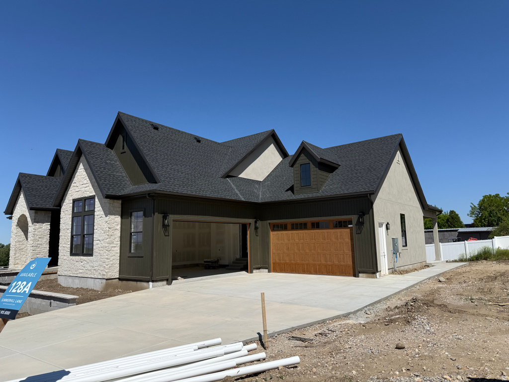 Newly constructed residence featuring a dark shingle roof, light-colored stone and stucco exterior, and a wood-finish garage door