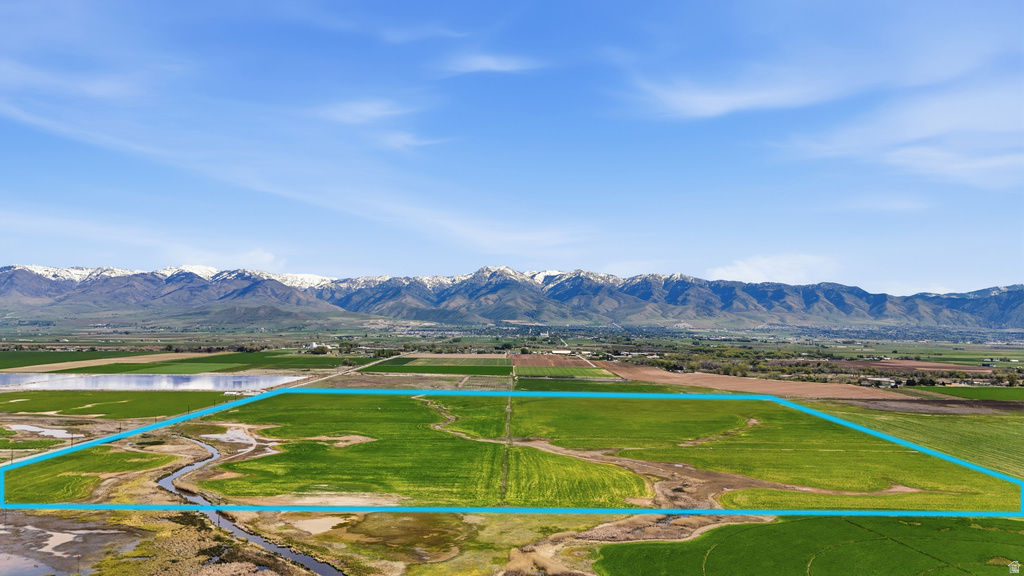 Expansive agricultural land featuring a natural water channel, visible mountain range backdrop, and clear sky