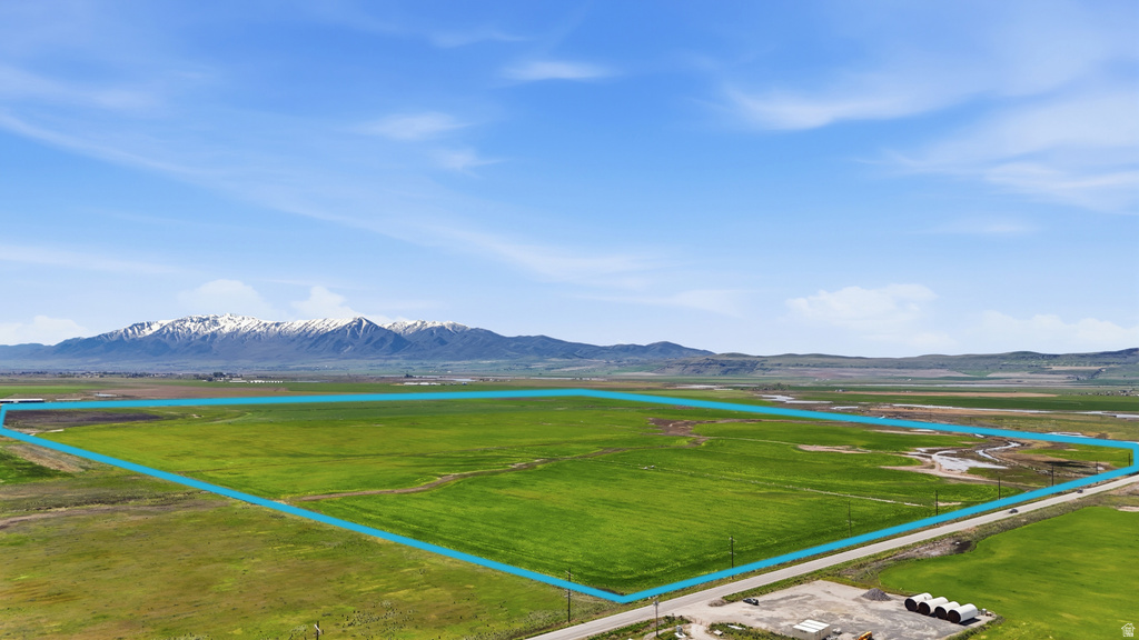 Expansive undeveloped land featuring a green field, a clear sky overhead, and distant mountains