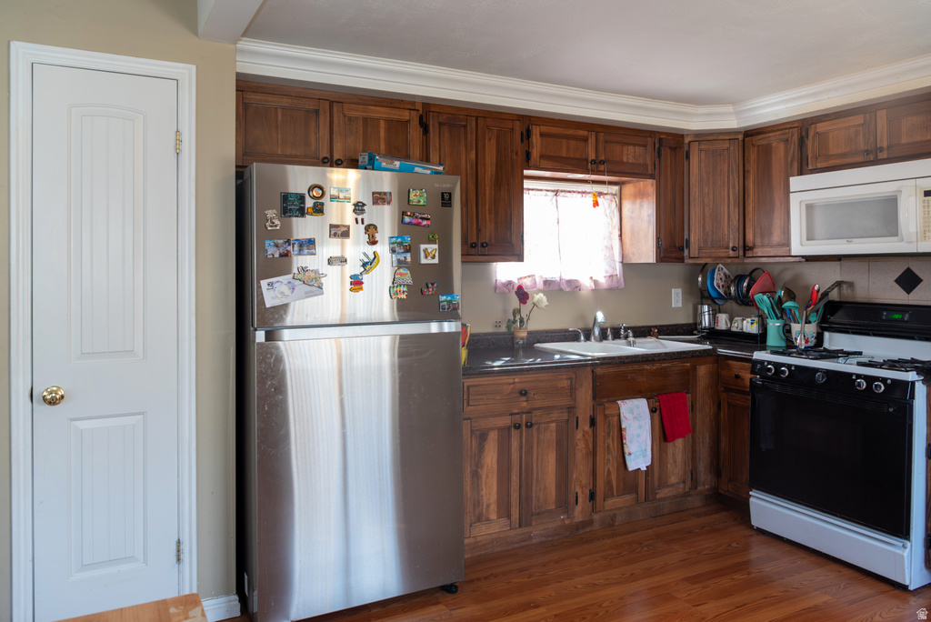 Kitchen with black gas stove, freestanding refrigerator, white microwave, dark countertops, and dark wood-style flooring