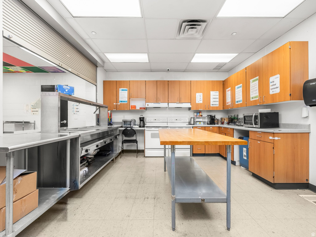 Kitchen with a paneled ceiling, white electric range, stainless steel microwave, stainless steel countertops, and dual tone cabinets