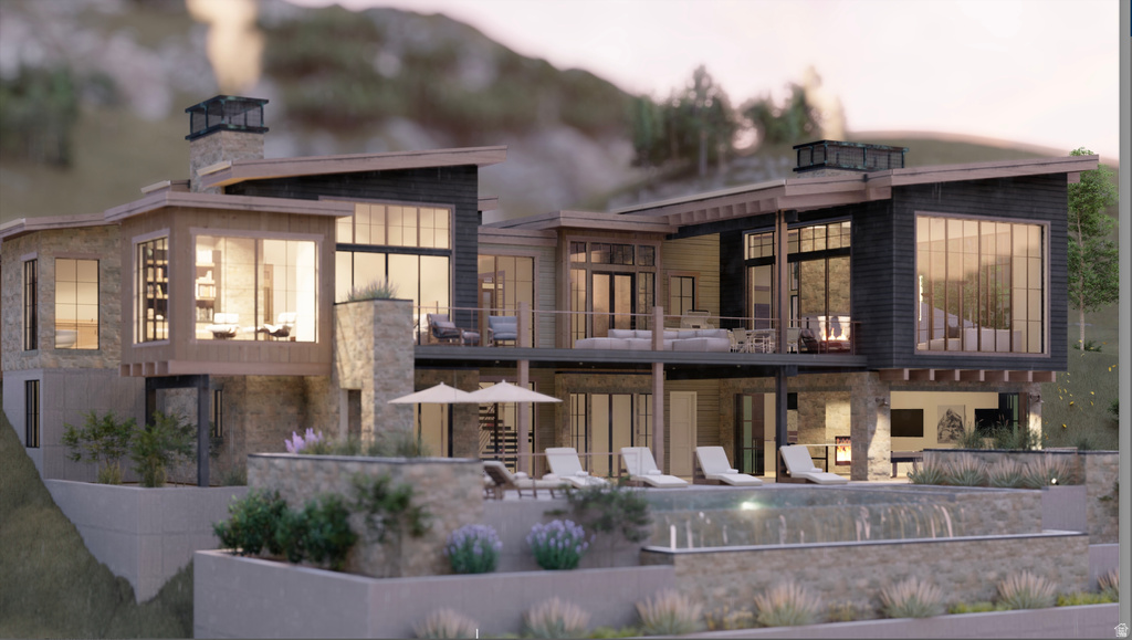 Back of house with a balcony, a chimney, stone siding, and a patio