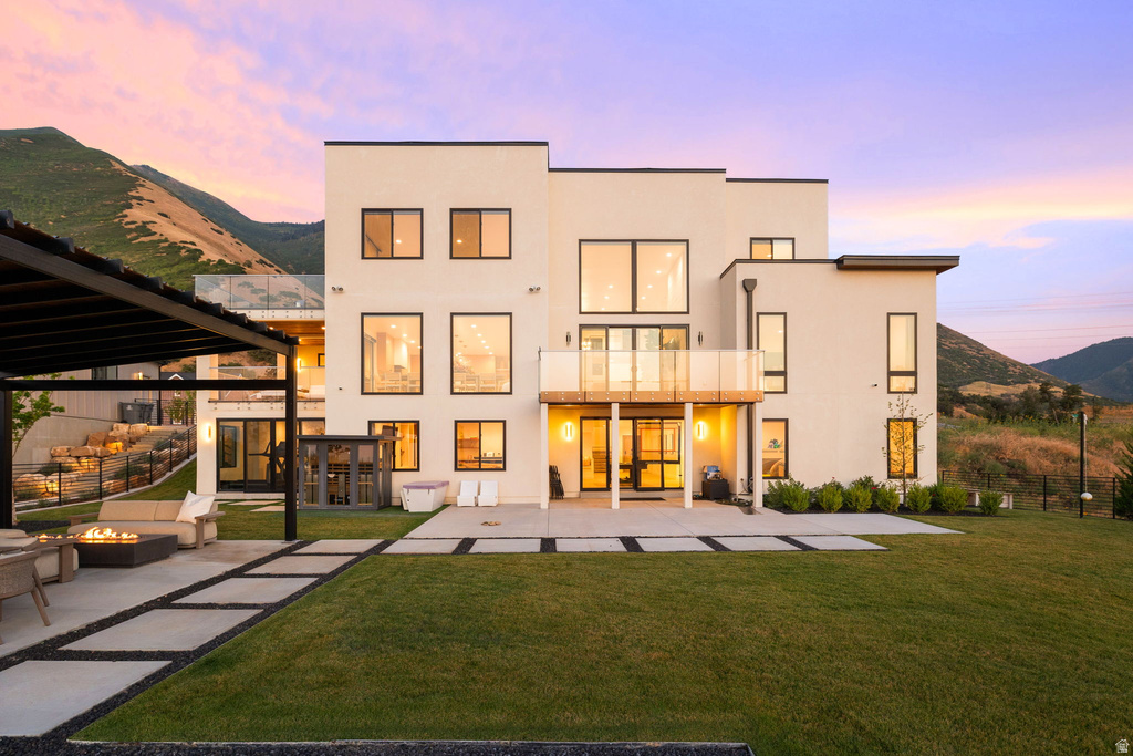 Back of property at dusk featuring a mountain view, a patio, an outdoor fire pit, and stucco siding