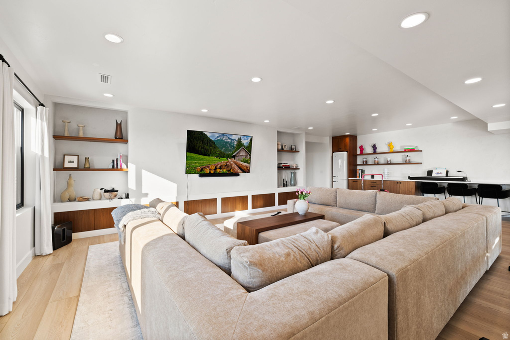 Living area featuring light wood-style flooring, built in shelves, recessed lighting, and bar area