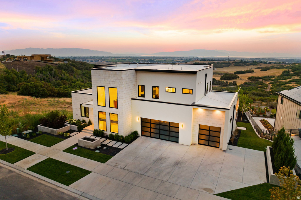 Modern home featuring concrete driveway, an attached garage, stucco siding, a mountain view, and a front lawn