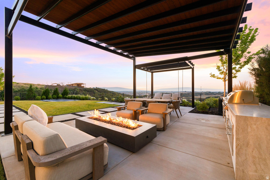 Patio terrace at dusk featuring an outdoor kitchen with living area, a lawn, a patio, a pergola, and a fire pit