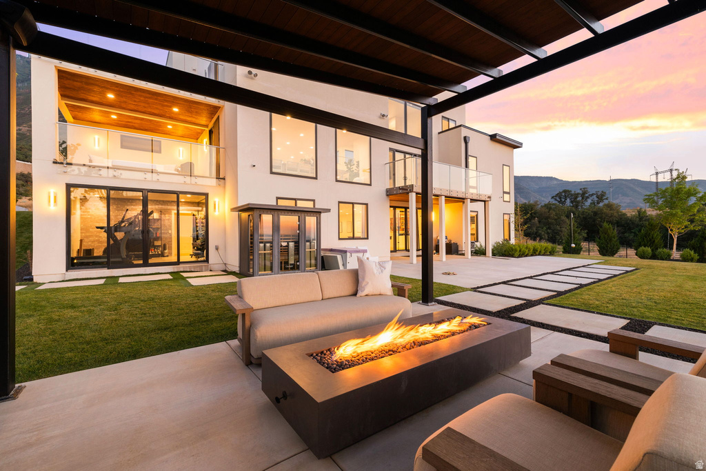 Rear view of house featuring a yard, a balcony, a patio area, stucco siding, and an outdoor living space with a fire pit