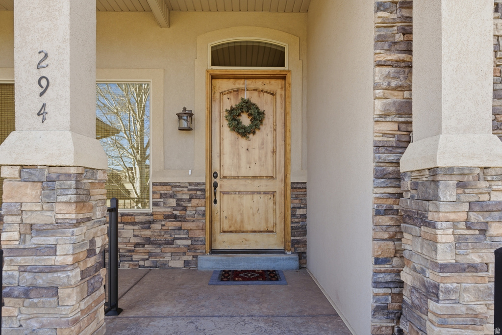 Entrance to property featuring stone siding, stucco siding, and covered porch