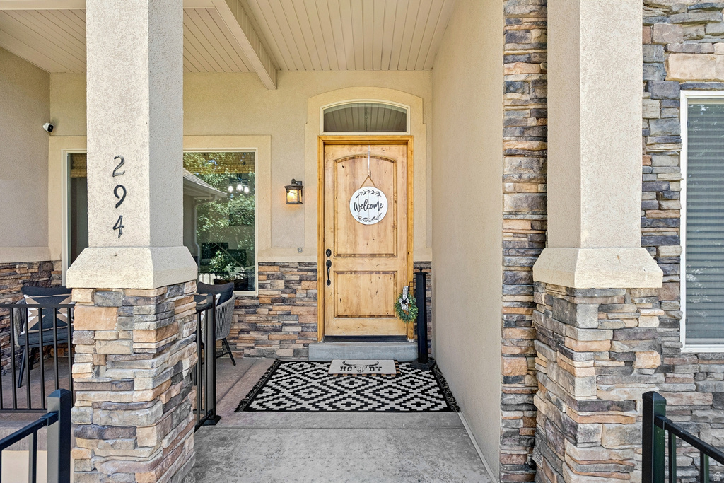 Doorway to property with stone siding, a porch, and stucco siding