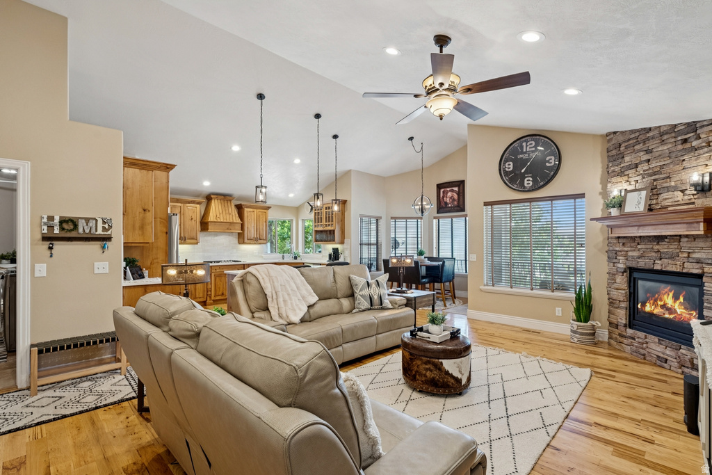Living room featuring ceiling fan, light wood-style flooring, a stone fireplace, vaulted ceiling, and recessed lighting