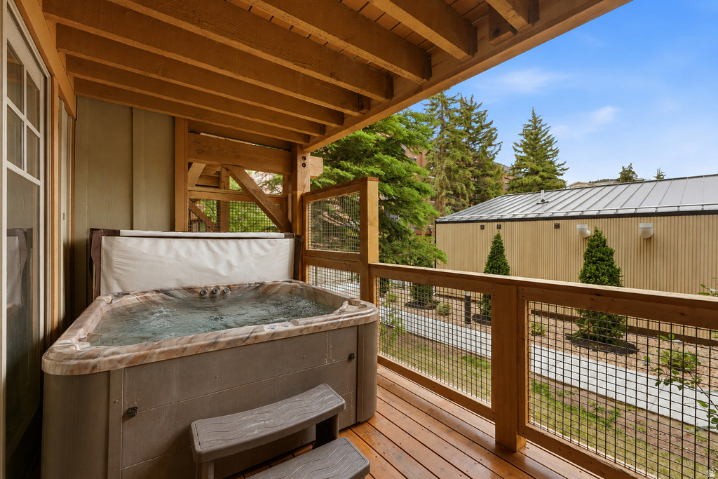 Covered outdoor balcony featuring a built-in spa, wood-finish decking, and robust wooden railings with wire mesh infill