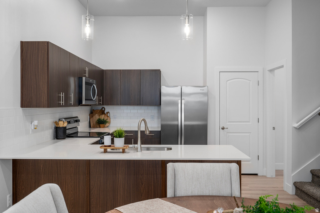 Kitchen featuring dark wood finish cabinetry, a peninsula, stainless steel appliances, modern cabinets, and light stone counters